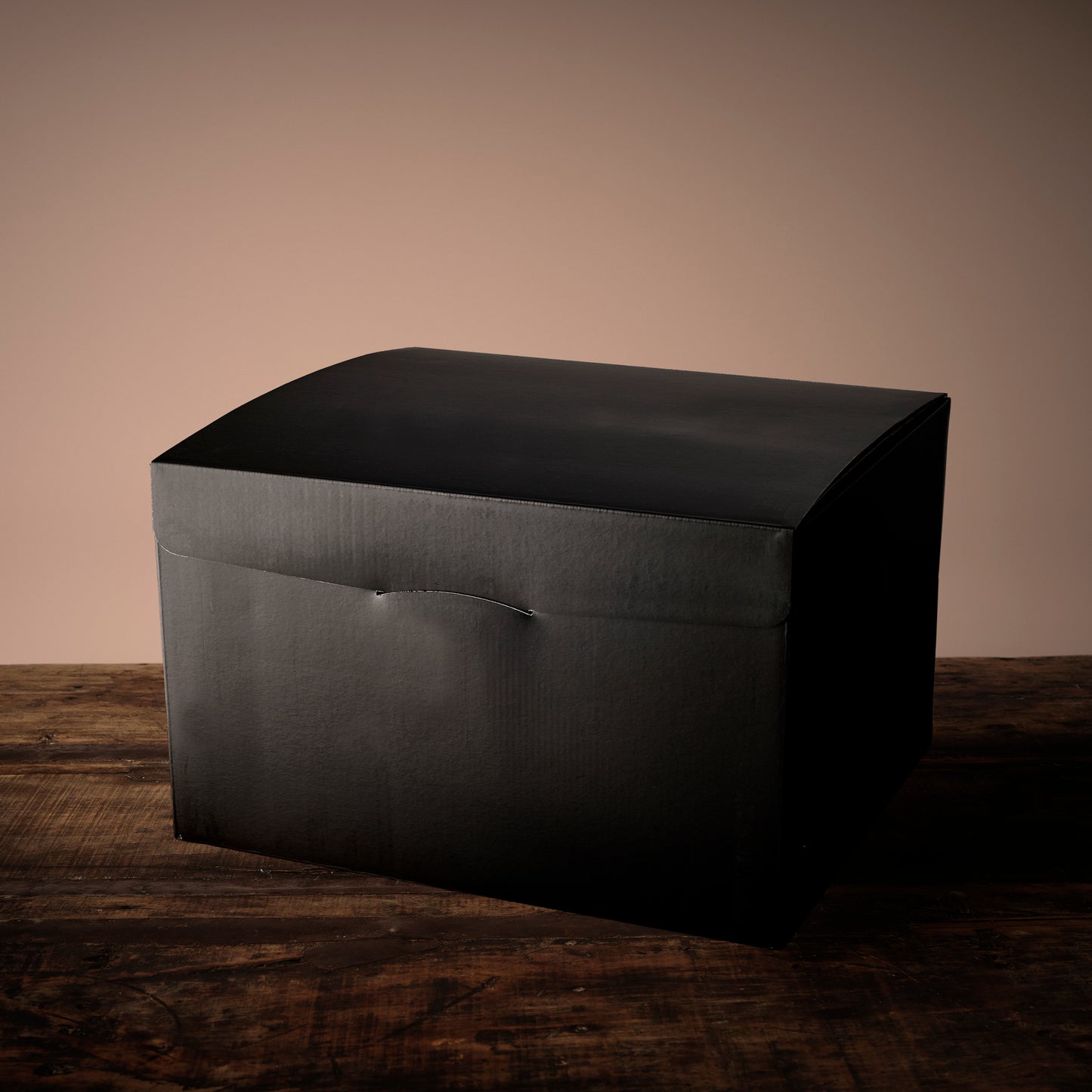 Side view of a matte black curved-lid gift box on a weathered wooden surface.