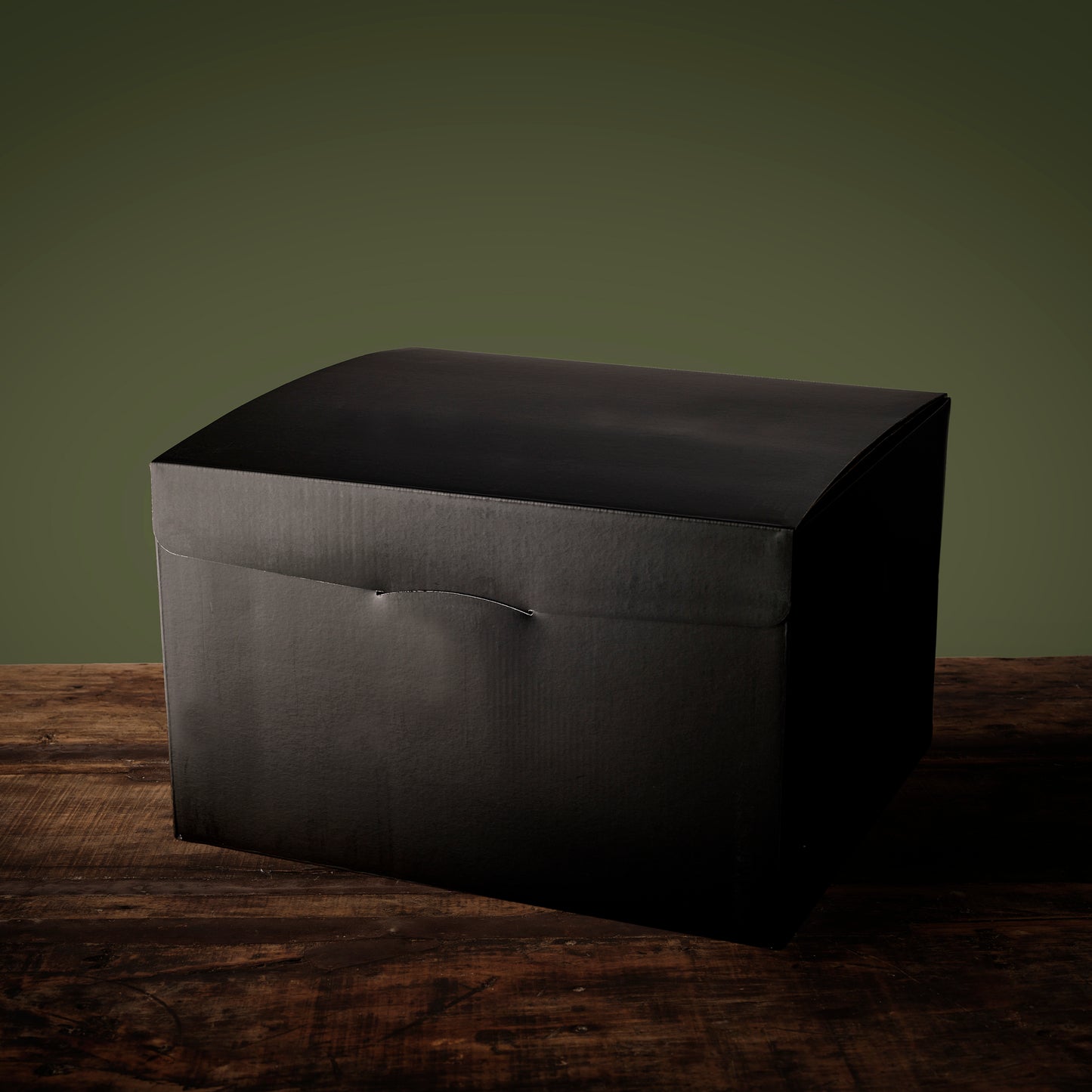 Elegant black gift box with a curved lid sits on a rustic wooden table
