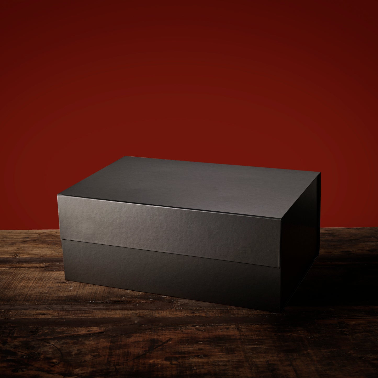 Matte black rectangular gift box on a rustic wooden table against a deep red background.