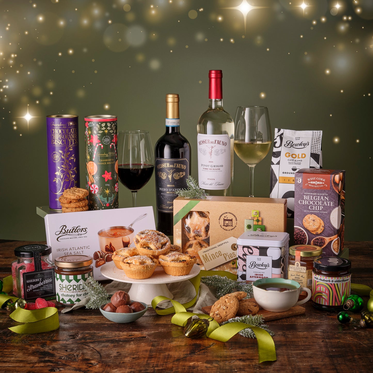 Gourmet gift set with wine, cookies, and other treats on a wooden table with a festive background.