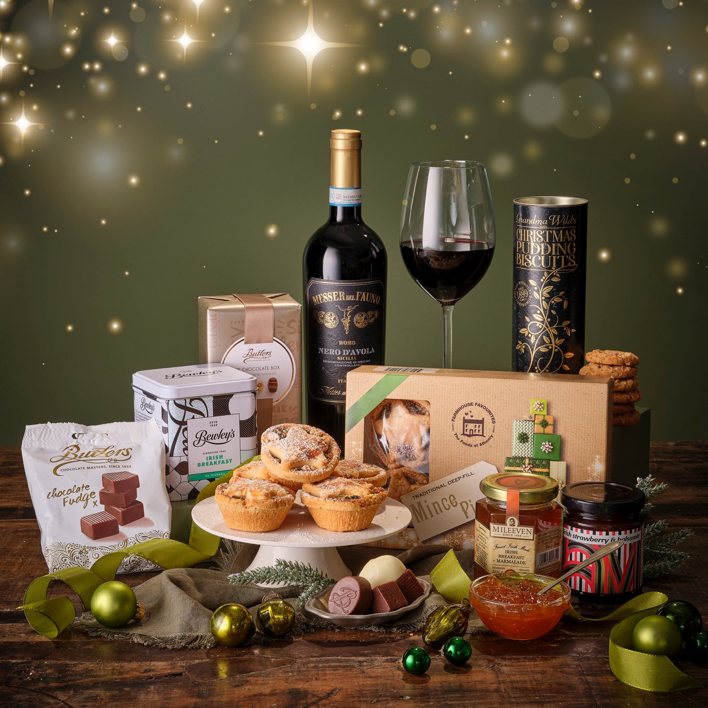 Gourmet gift set with wine, pastries, and other treats on a wooden table with a festive background.