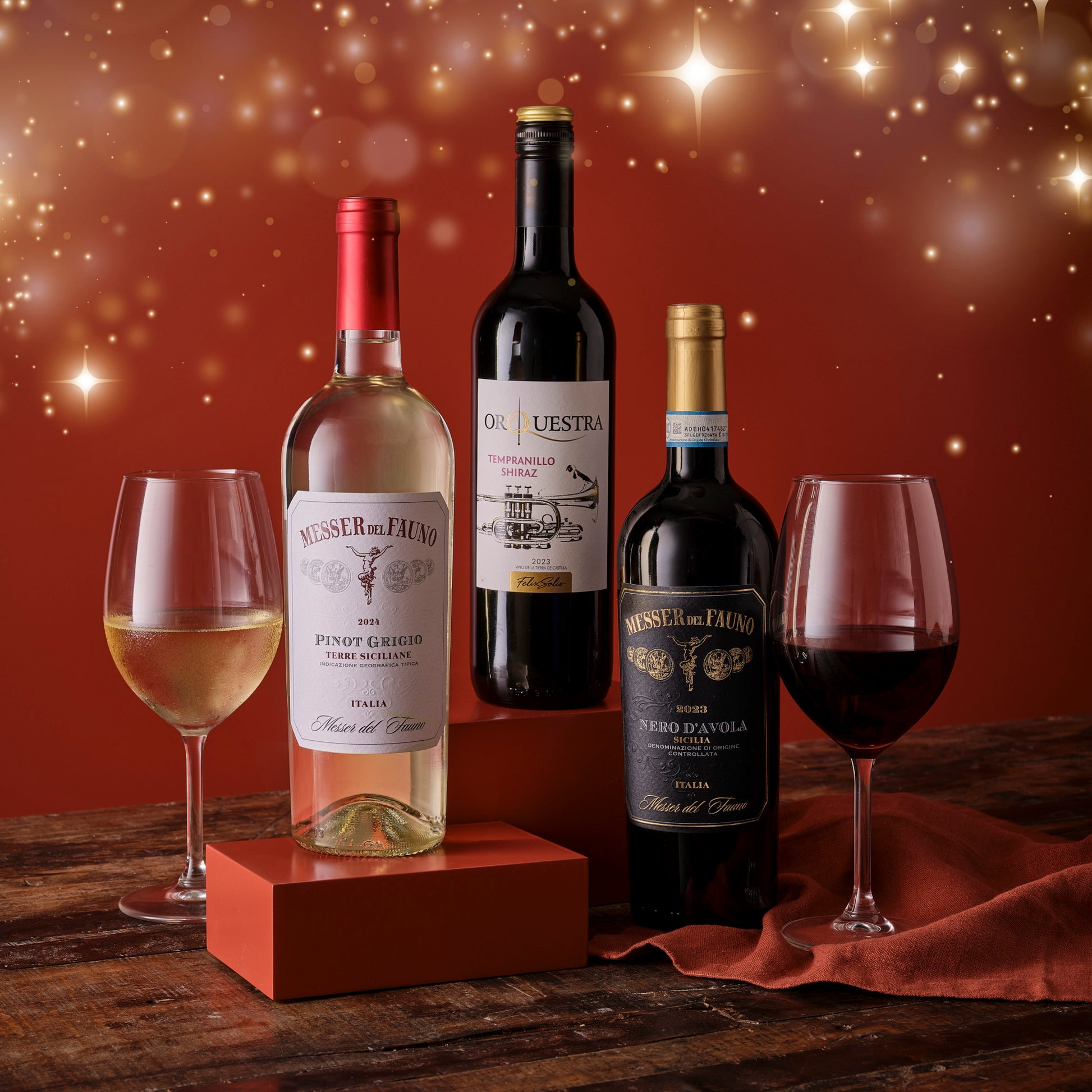 Three bottles of wine with glasses on a wooden surface against a warm, blurred background