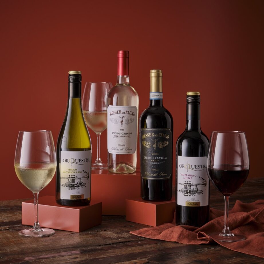 Four wine bottles with two glasses on a rustic wooden surface against a warm red background.