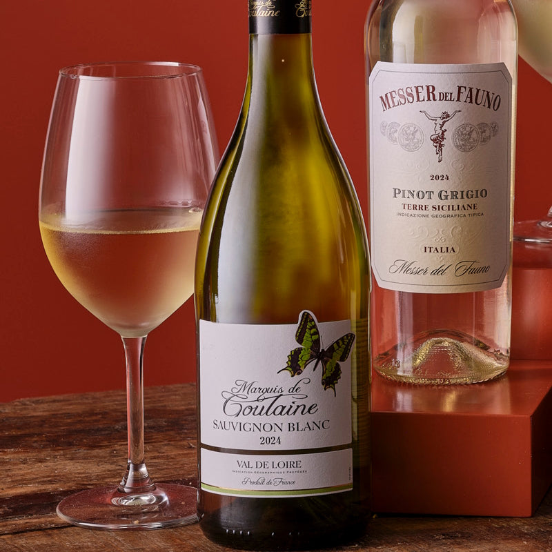 Two wine bottles and a glass of wine on a wooden surface with a red background