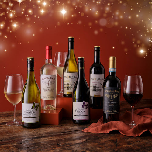 Assorted wine bottles and glasses on a wooden surface with a festive background
