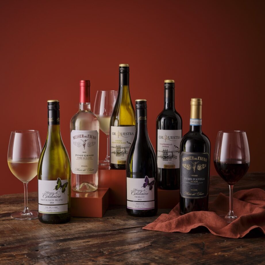 Assortment of red and white wine bottles with glasses on a wooden surface with a warm red background