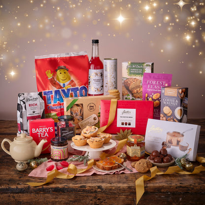 Assorted food products including tarts, jars, and a teapot on a wooden table with a festive background.