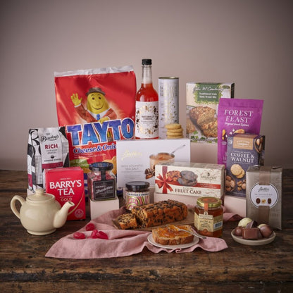 Feast from Home hamper with assorted biscuits jams cake and beverages arranged on a wooden table