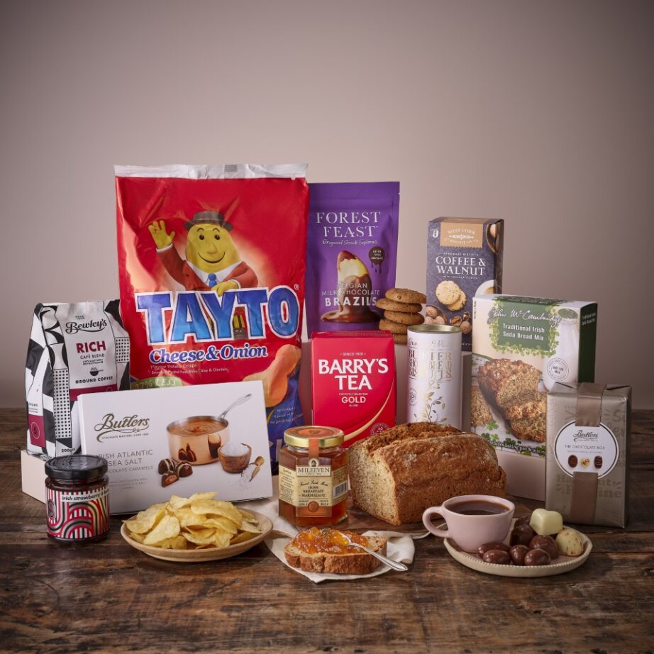 Abundant home hamper with bread jam crackers tea chocolates and snacks arranged on a rustic wooden table