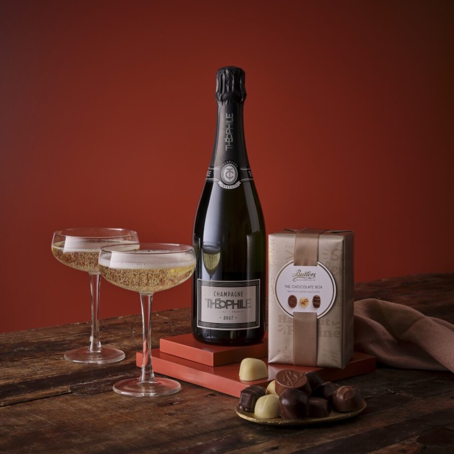 Champagne Brut gift set with two glasses, a central champagne bottle, and a chocolate box on a rustic wooden table