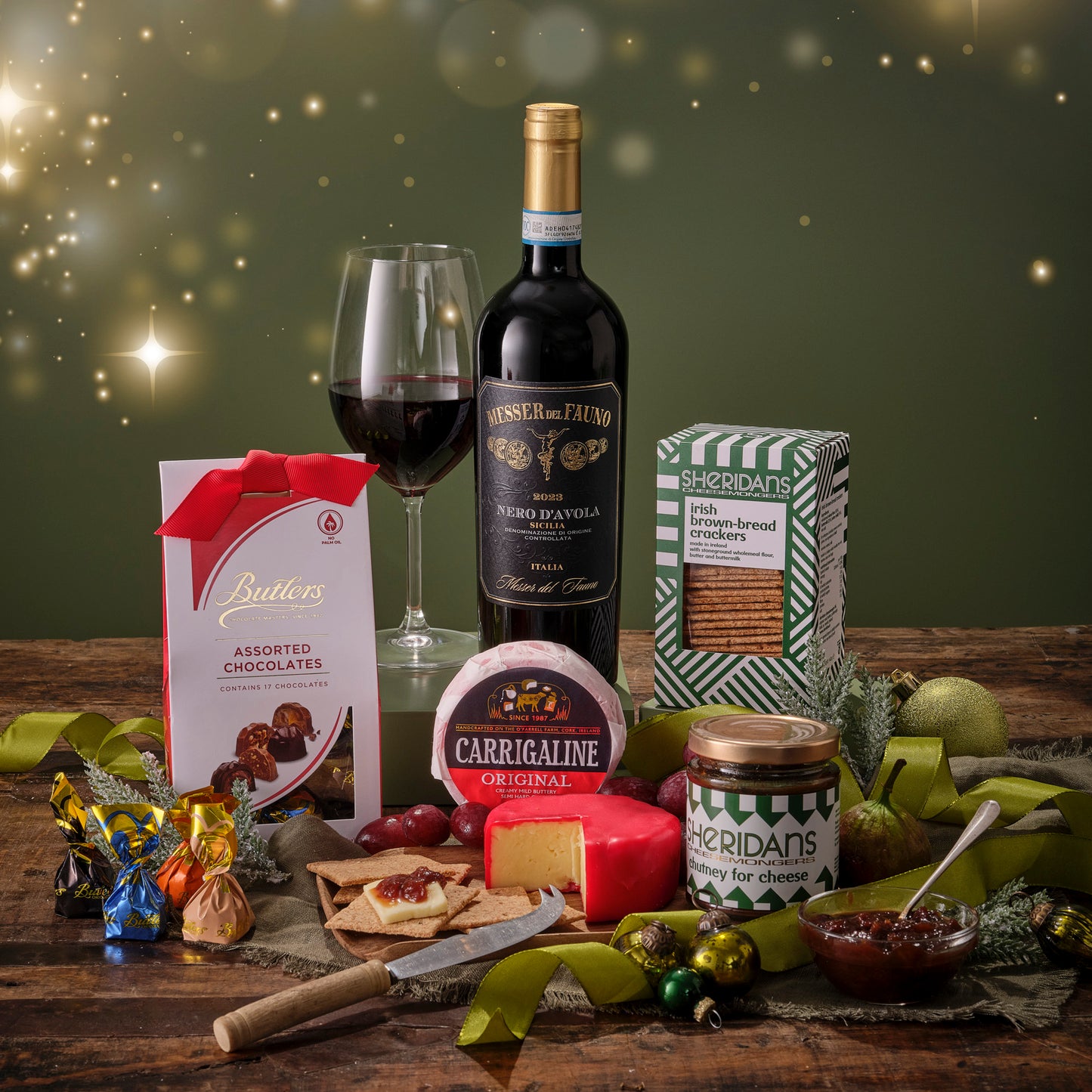 Gourmet gift set with wine, chocolates, and assorted foods on a wooden table.