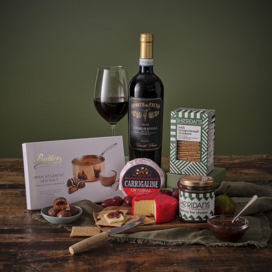 Gourmet gift set with wine, cheese, and snacks on a wooden table.