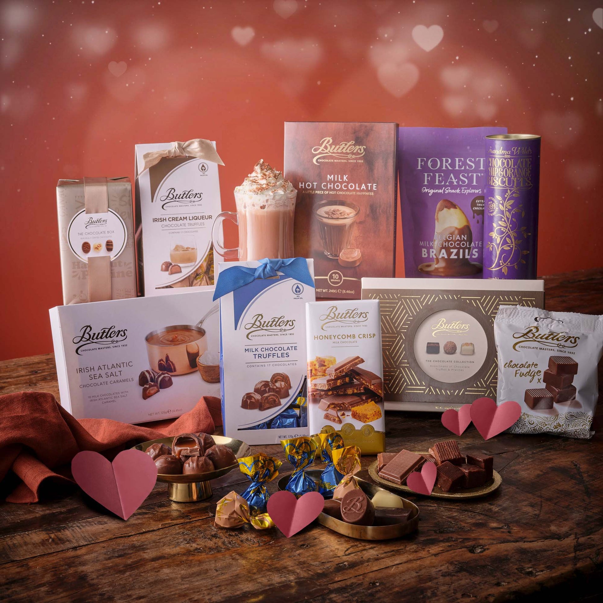 Romantic chocolate hamper including a candle bow wrapped box and assorted chocolates on a pink backdrop.