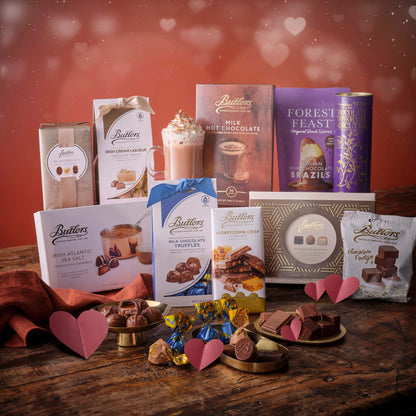 Romantic chocolate hamper including a candle bow wrapped box and assorted chocolates on a pink backdrop.