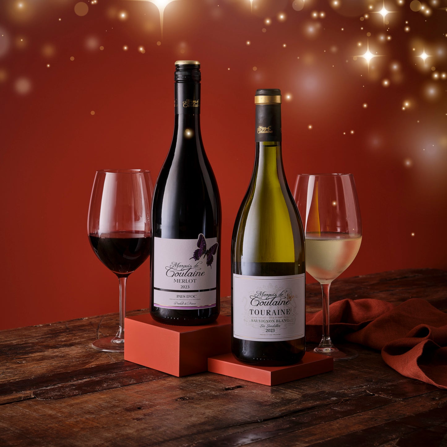 Two wine bottles with glasses on a wooden surface against a warm, blurred background