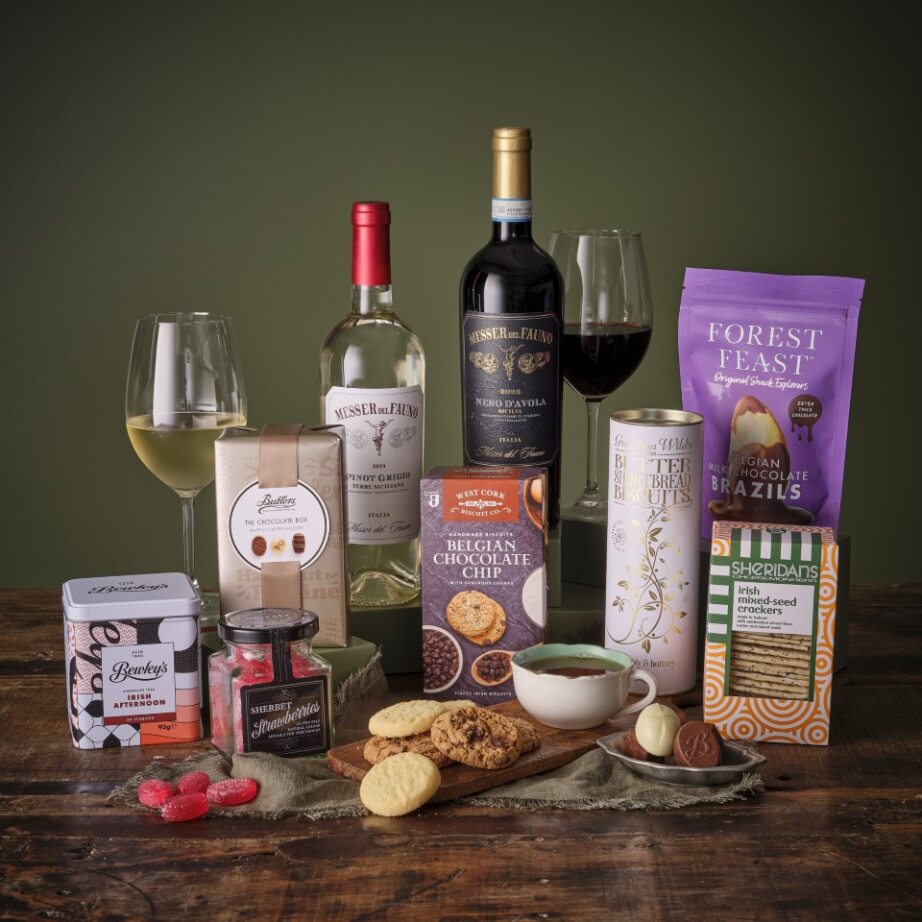 From Me to You Hamper gift set featuring two wine bottles, chocolates, biscuits, jam, and other snacks on a wooden table.