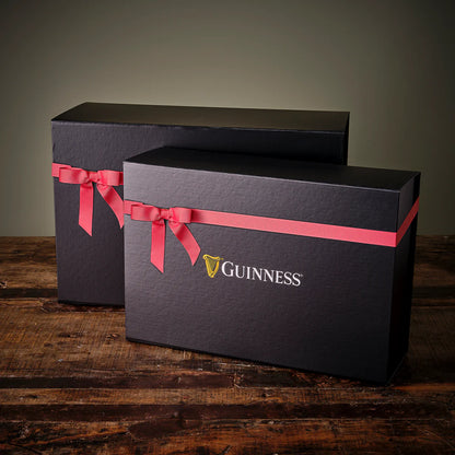 Two black gift boxes with red ribbons on a wooden surface, featuring the Guinness logo.