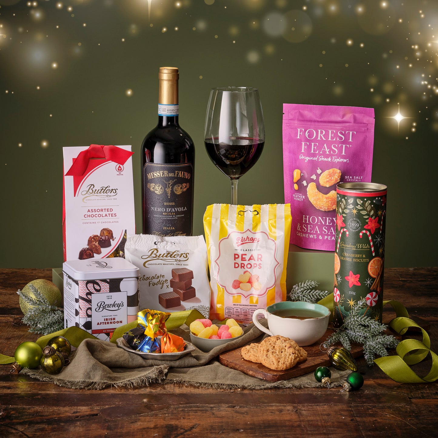 Gourmet gift set with wine, chocolate, and snacks on a wooden table with a festive background.