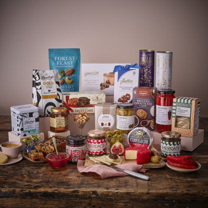 Gourmet Selection Hamper assortment featuring a white gift box with blue ribbon surrounded by chocolates biscuits and jars.