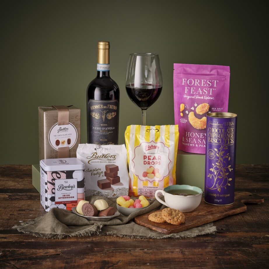 Gourmet Treats Hamper includes a bottle of wine, cookies chocolates and a variety of snacks arranged on a wooden table.