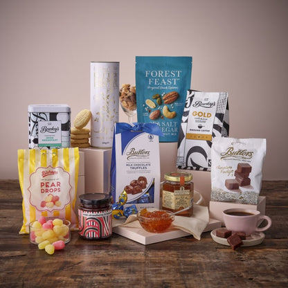 Assorted snacks and treats arranged for Grandma's Kitchen Hamper on a wooden surface including tea tins and biscuits