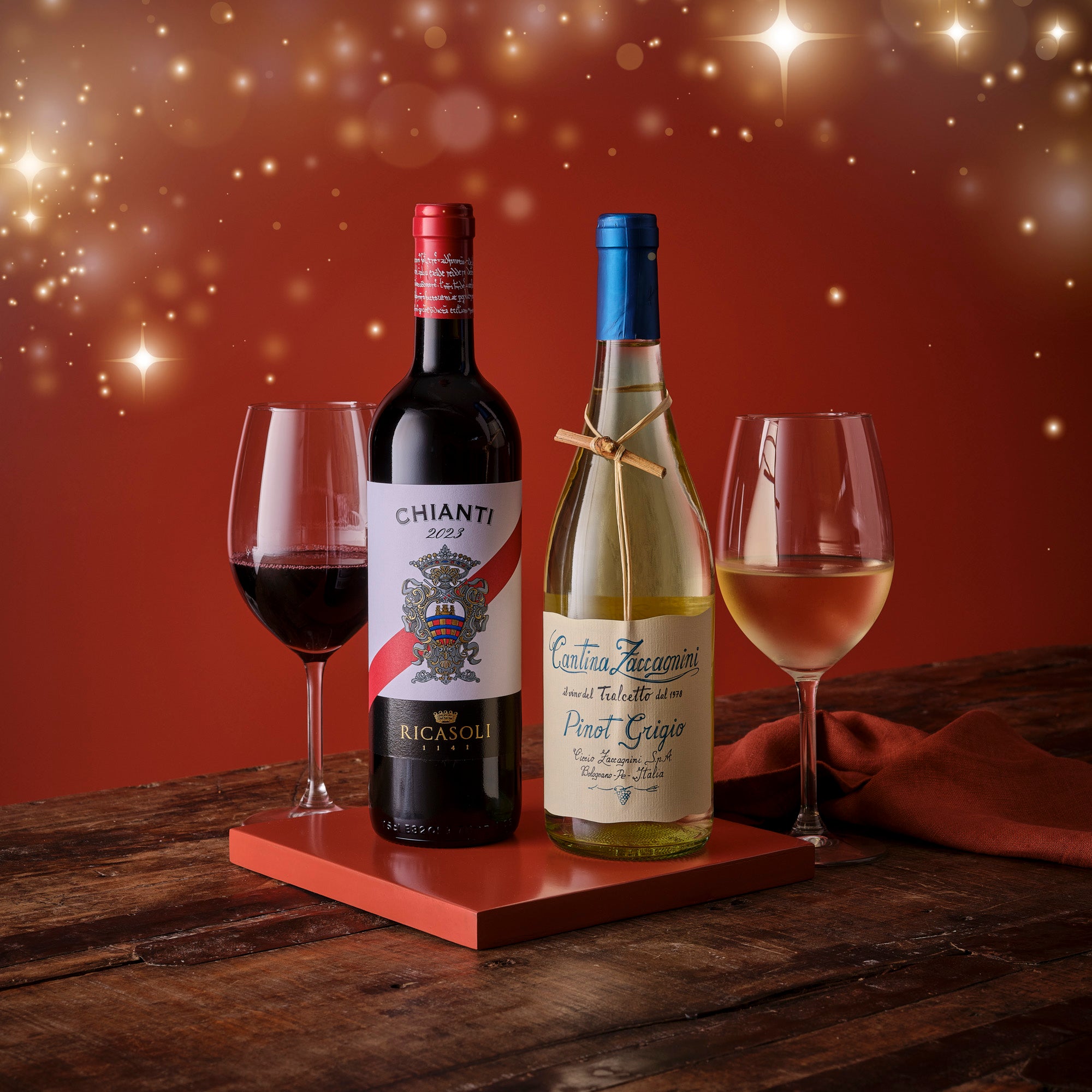 Two wine bottles with glasses on a wooden surface against a warm, glowing background