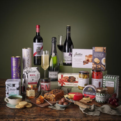Luxurious food and drink hamper spread with wine bottles, chocolate bars, jars, and snacks on a rustic wooden table