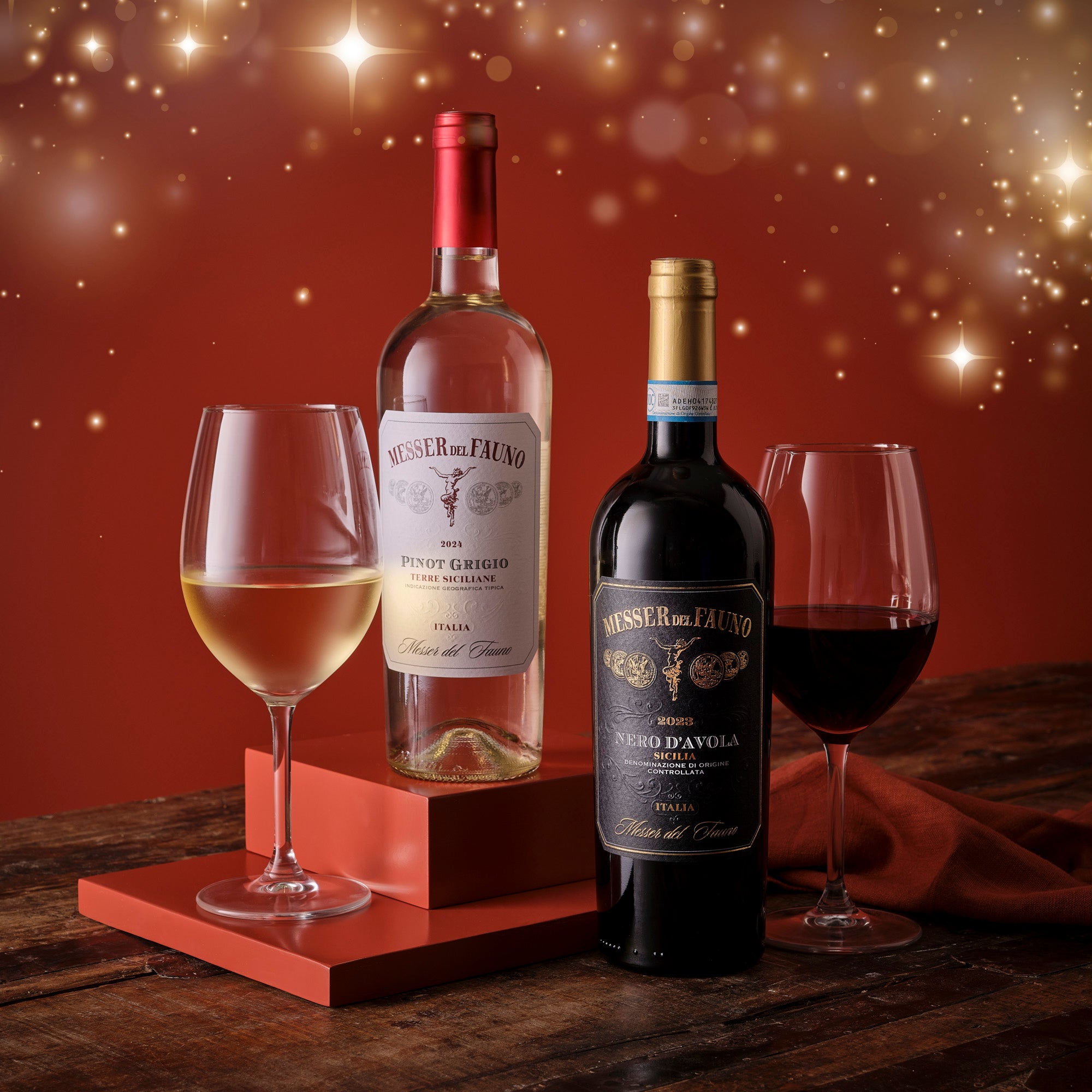 Two bottles of wine with glasses on a wooden surface against a warm, glowing background.
