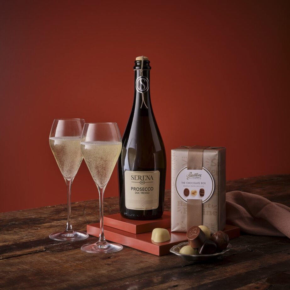 Prosecco and chocolate gift set with a Serena Prosecco bottle, two fluted glasses, and chocolates on a wooden surface