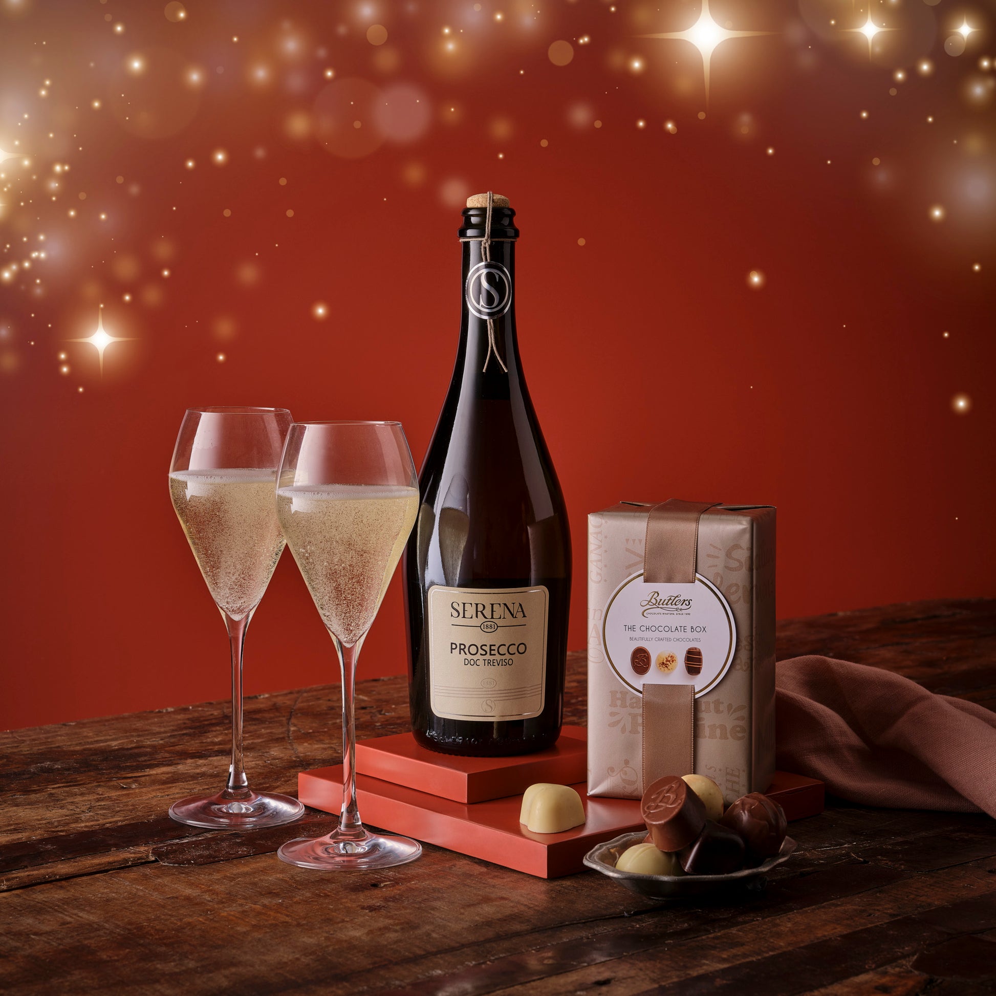 Bottle of Prosecco with two glasses and chocolate truffles on a wooden table with a festive background.