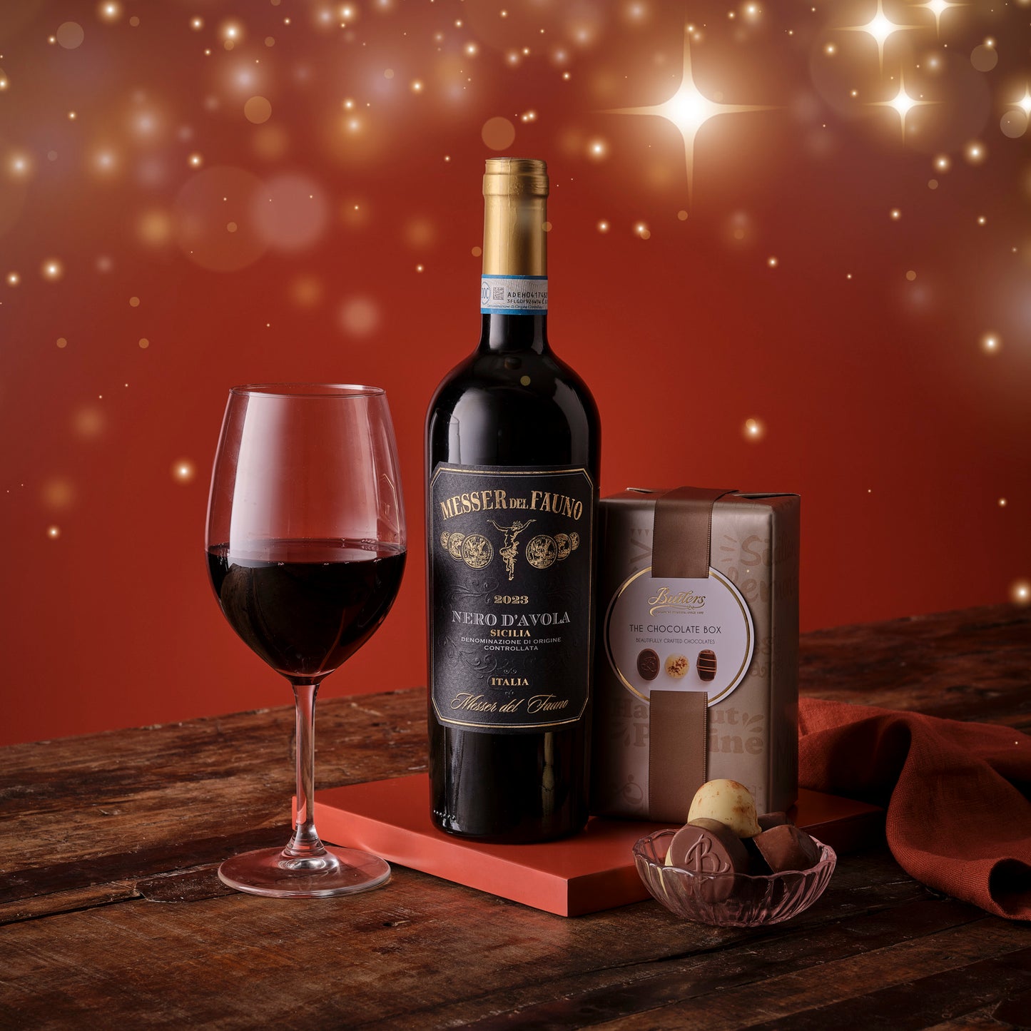 Bottle of wine, glass, and chocolate truffles on a wooden table with a warm, glowing background.