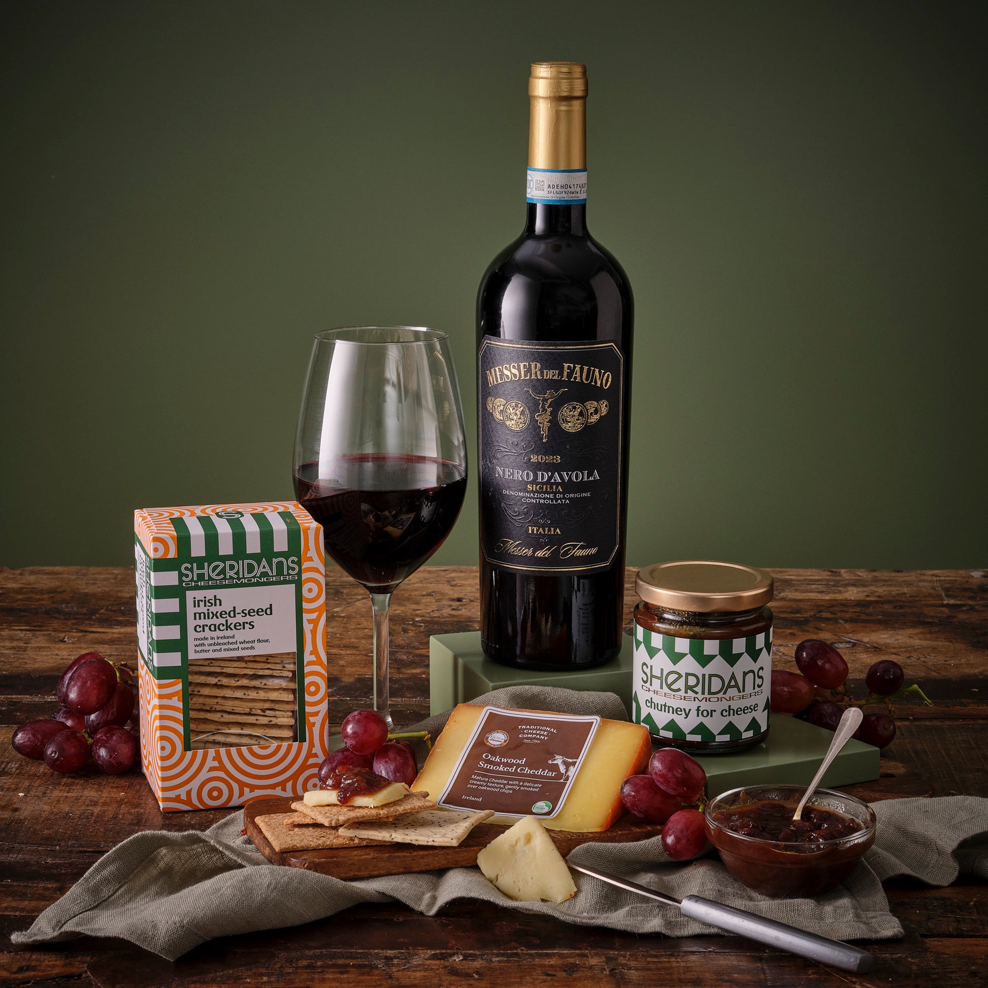 Red Wine bottle, glass, and assorted snacks on a wooden table with a green background