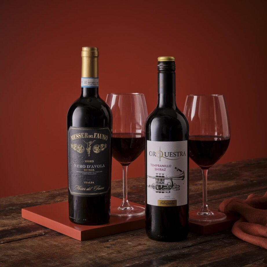 Two red wine bottles with glasses on a wooden surface against a warm, glowing background