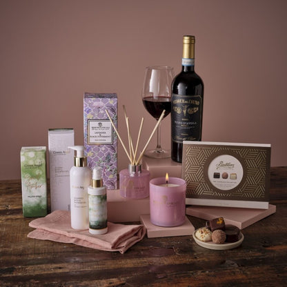 Self care pamper hamper with lavender products, candle, diffuser, chocolates and a wine bottle on a wooden table.