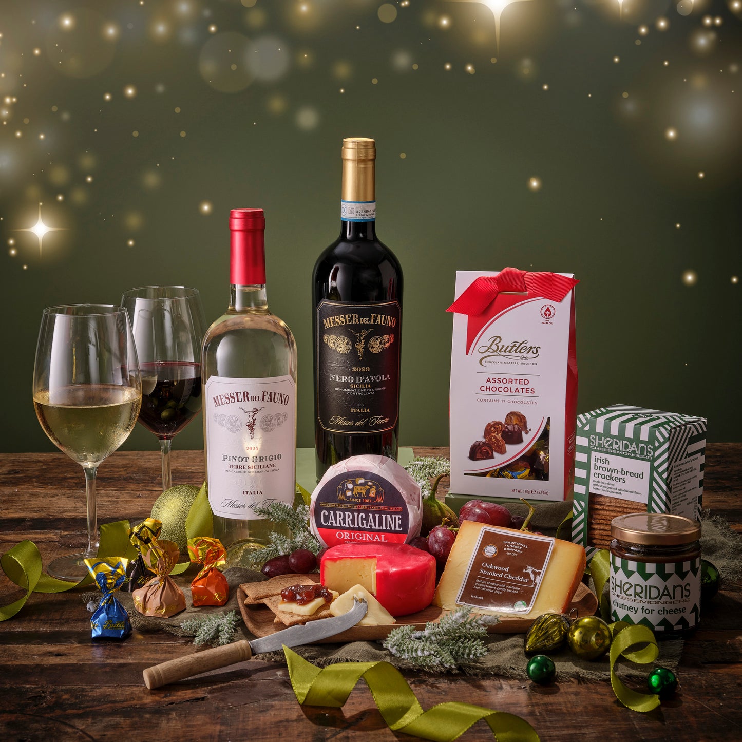 Wine bottles, cheese, and chocolate on a wooden table with a festive background