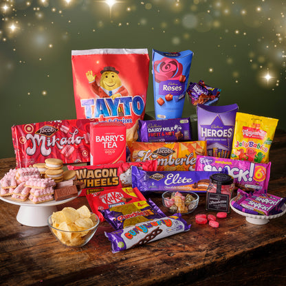 Assorted Irish snacks, Barry's Tea, Cadburys Roses, Tayto, Maynards jellies, wagon wheels, and Jacobs biscuits  on a wooden table with a festive background.