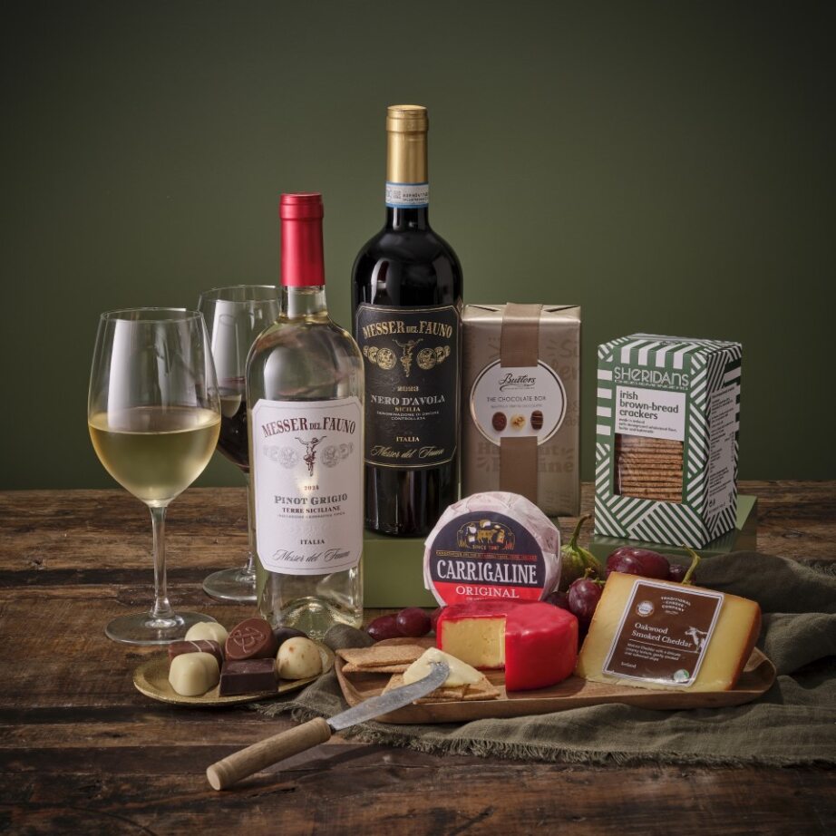 The Essentials Hamper includes wine cheese crackers and chocolates arranged on a rustic wooden board.