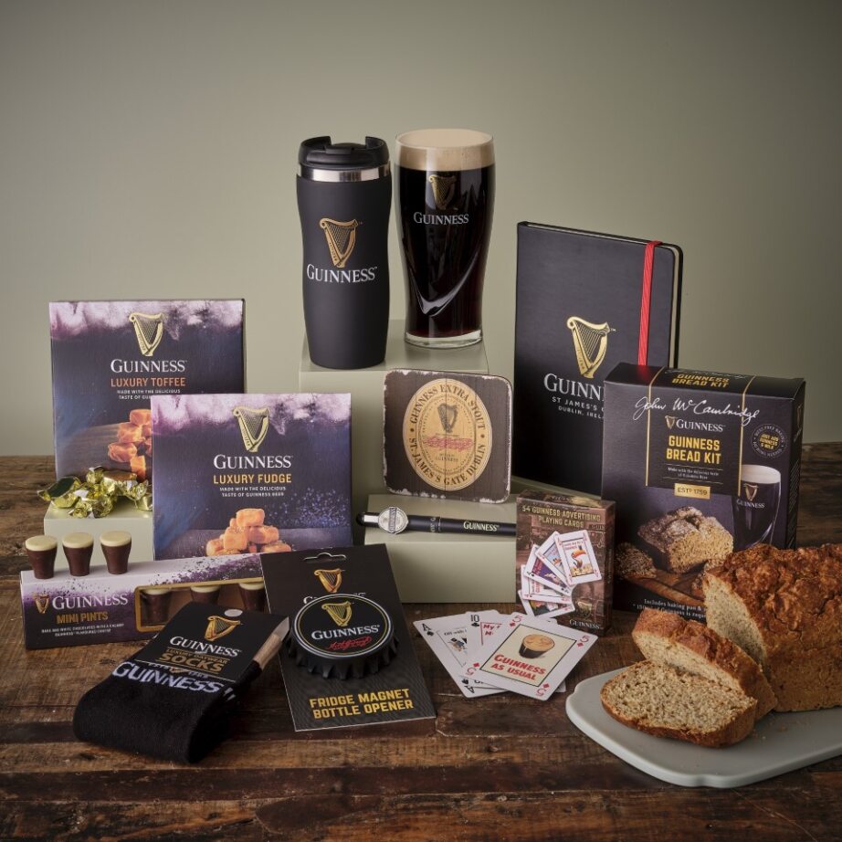 Guinness themed gift hamper featuring a pint glass, black travel mug, and a spread of boxed snacks and accessories.