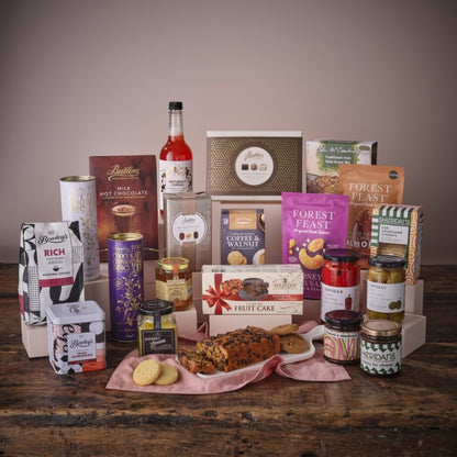 The Grand Gourmet Hamper with chocolates biscuits jars and a bottle arranged on a rustic wooden table.