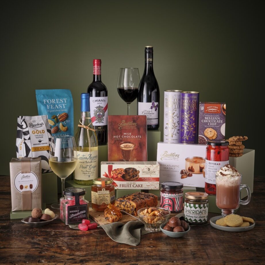 The Ultimate Sweet and Savoury Hamper featuring wine, chocolates, jars and snacks arranged on a wooden table.