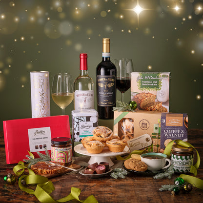 Gourmet gift set with wine, pastries, and other treats on a wooden table with a festive background.