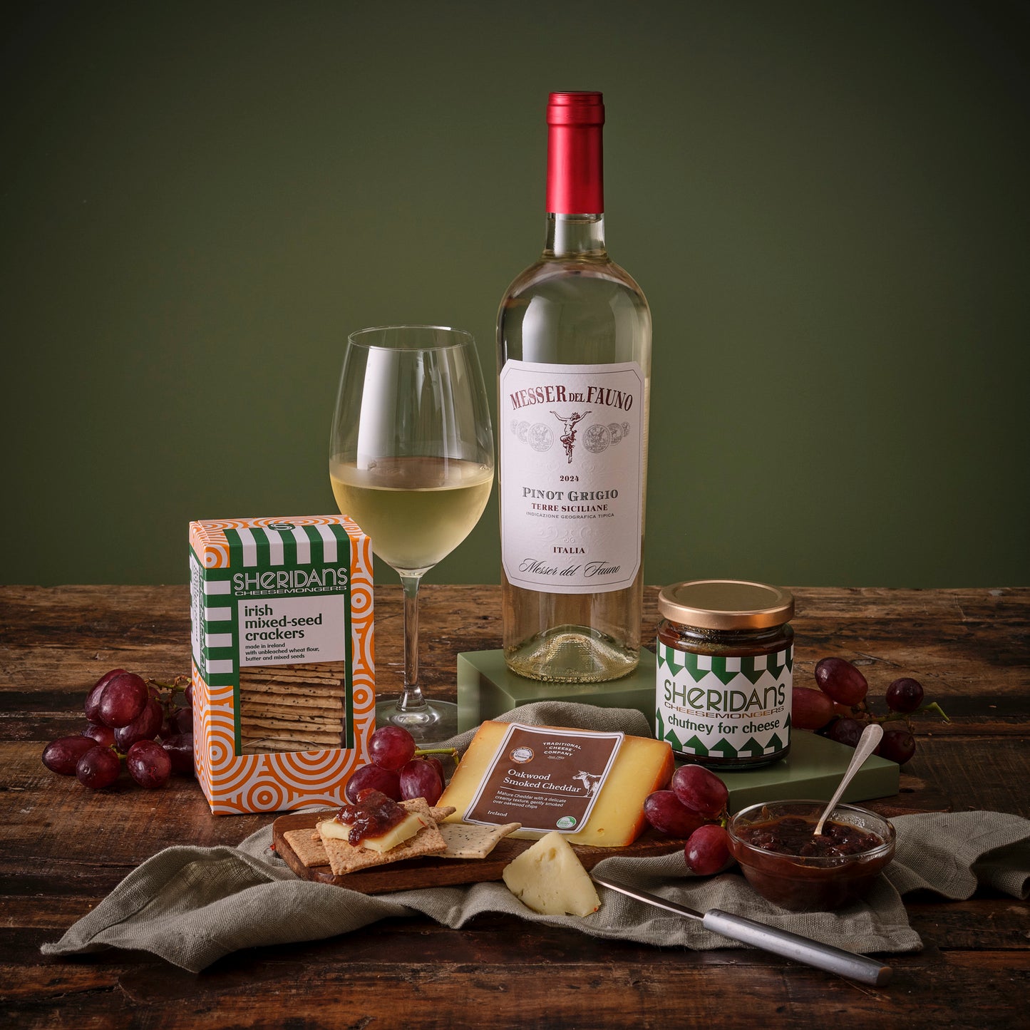 White Wine bottle, glass, and assorted snacks on a wooden table with a green background