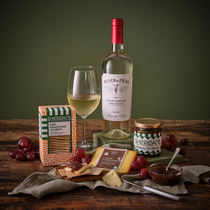 White Wine bottle, glass, and assorted snacks on a wooden table with a green background