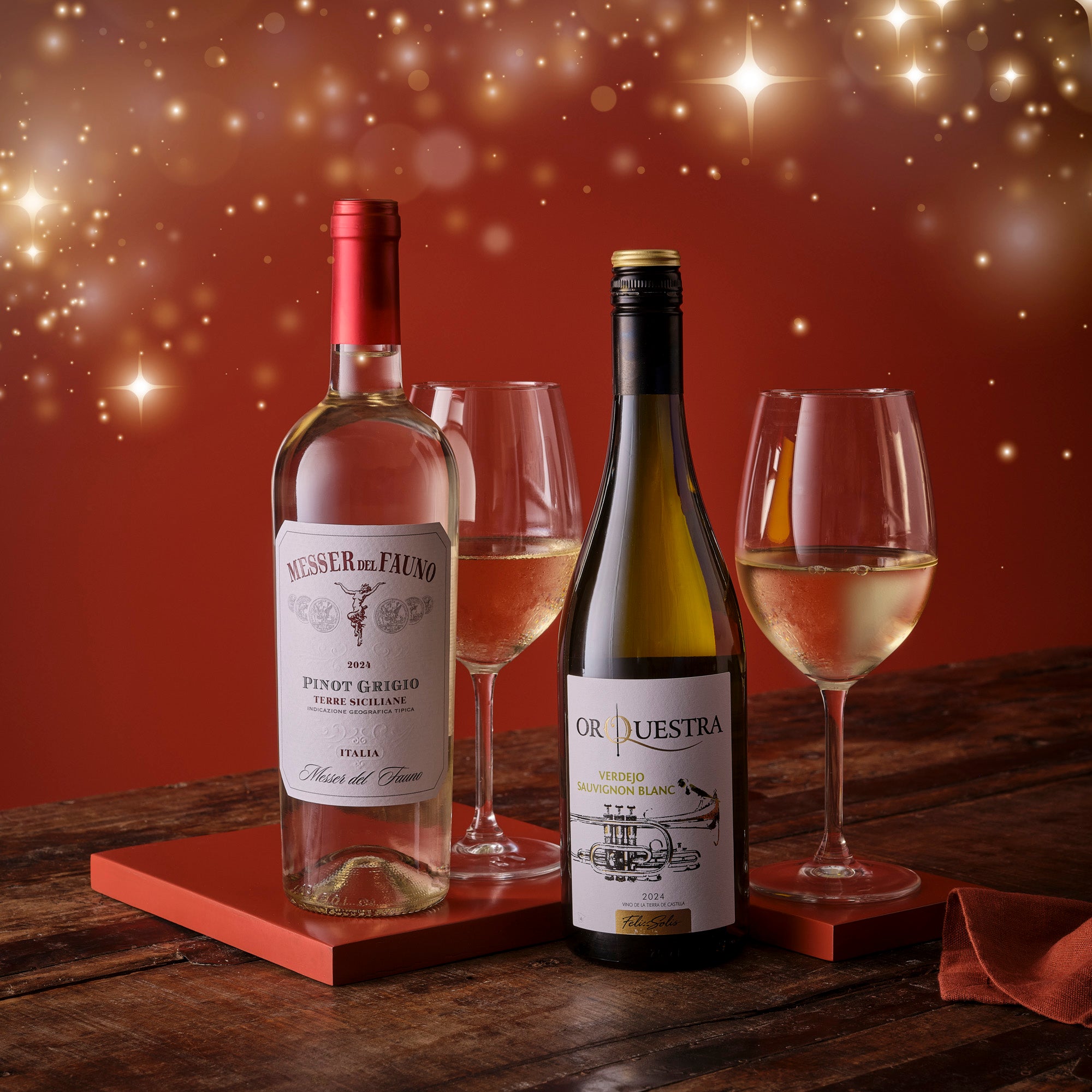 Two wine bottles with glasses on a wooden surface against a warm, glowing background