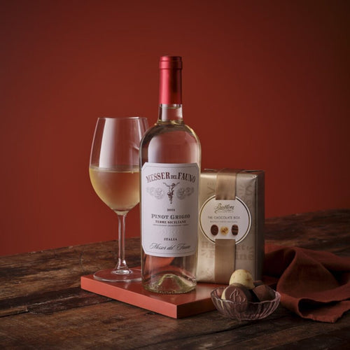 White wine and chocolate set featuring a Pinot Grigio bottle a glass and a chocolate box on a rustic wooden table