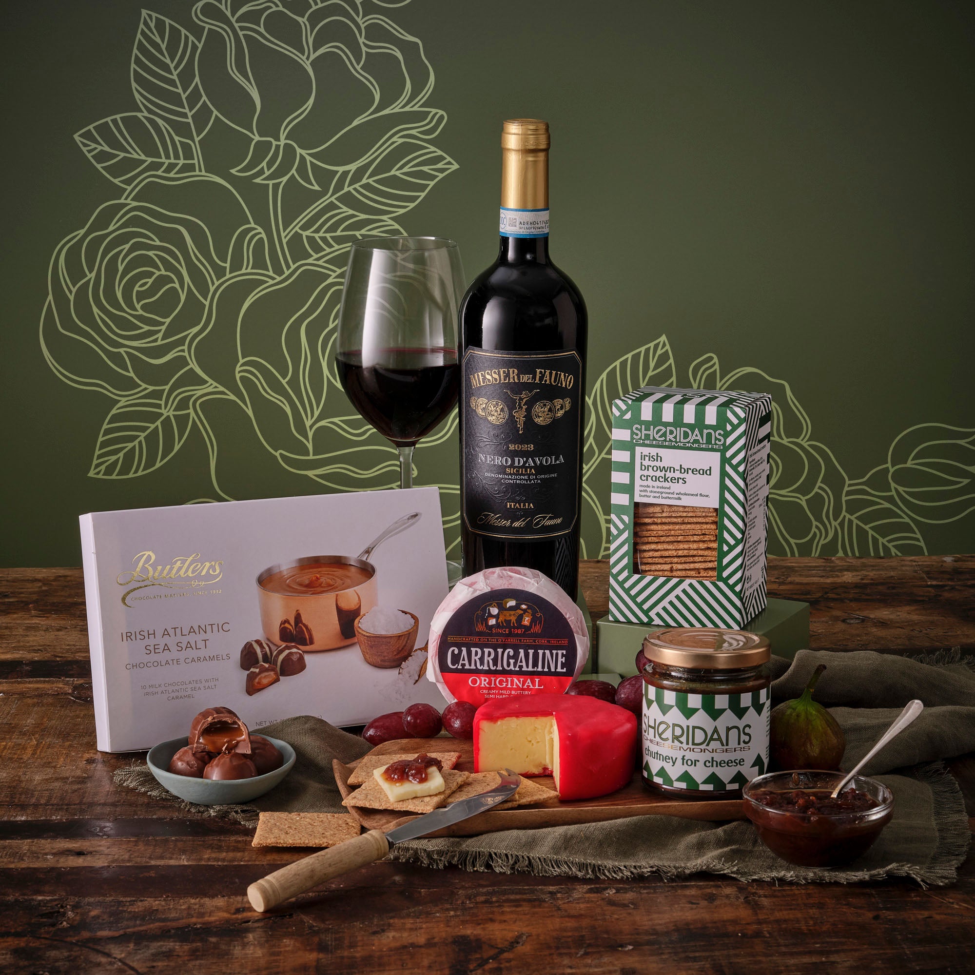 Mother's Day Cheese and Wine Hamper features a bottle of red wine, crackers, cheese and chutney on a rustic table.