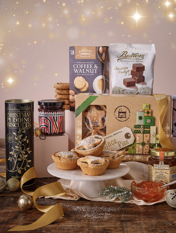 Assorted festive food items including pies, cookies, and tins on a wooden table with a soft, warm background.
