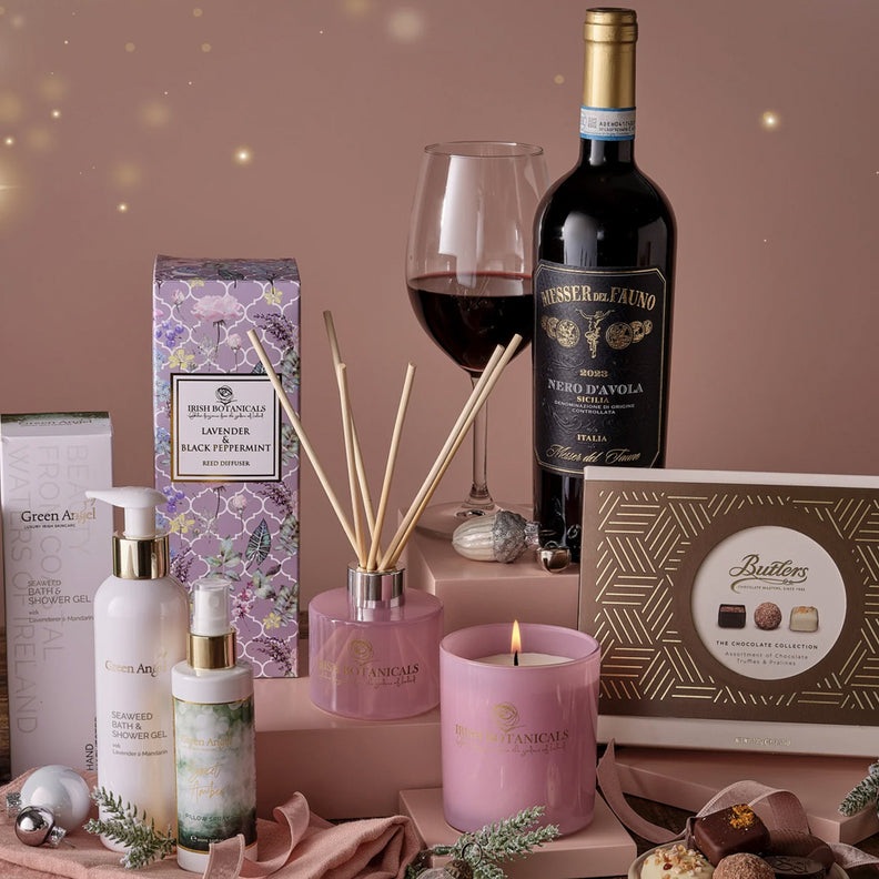 Gourmet gift set with wine, candles, and other items on a wooden surface.