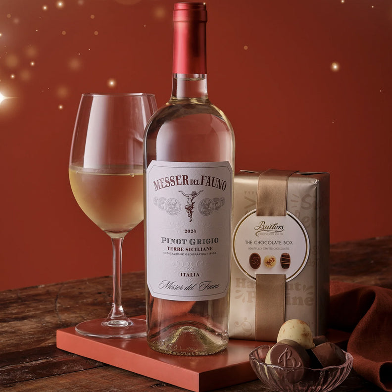 Wine bottle with a glass of wine and a chocolate box on a wooden table with a warm background.