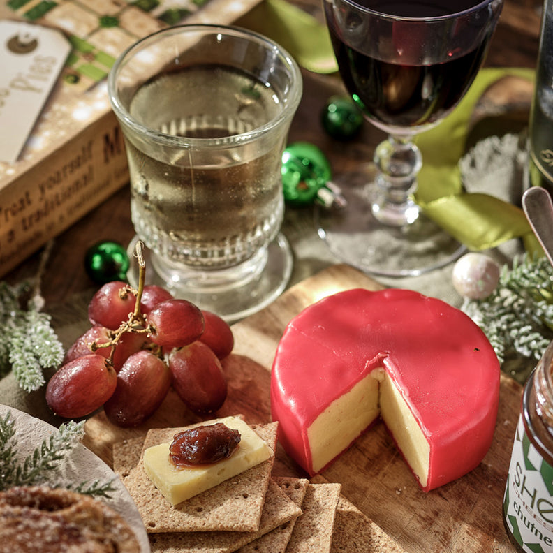 Table setting with a cheeseboard, wine, and assorted snacks on a wooden surface.